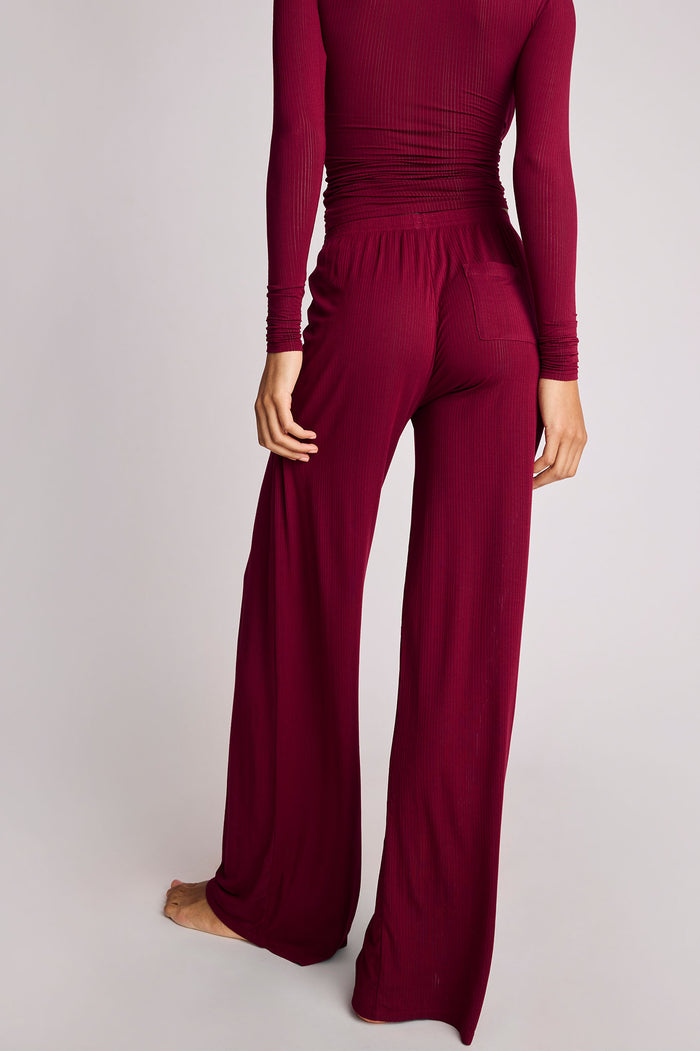 A person shown from the back wearing a matching long-sleeve ribbed top and wide-leg pants in a deep burgundy or wine color, photographed against a plain light gray studio background.