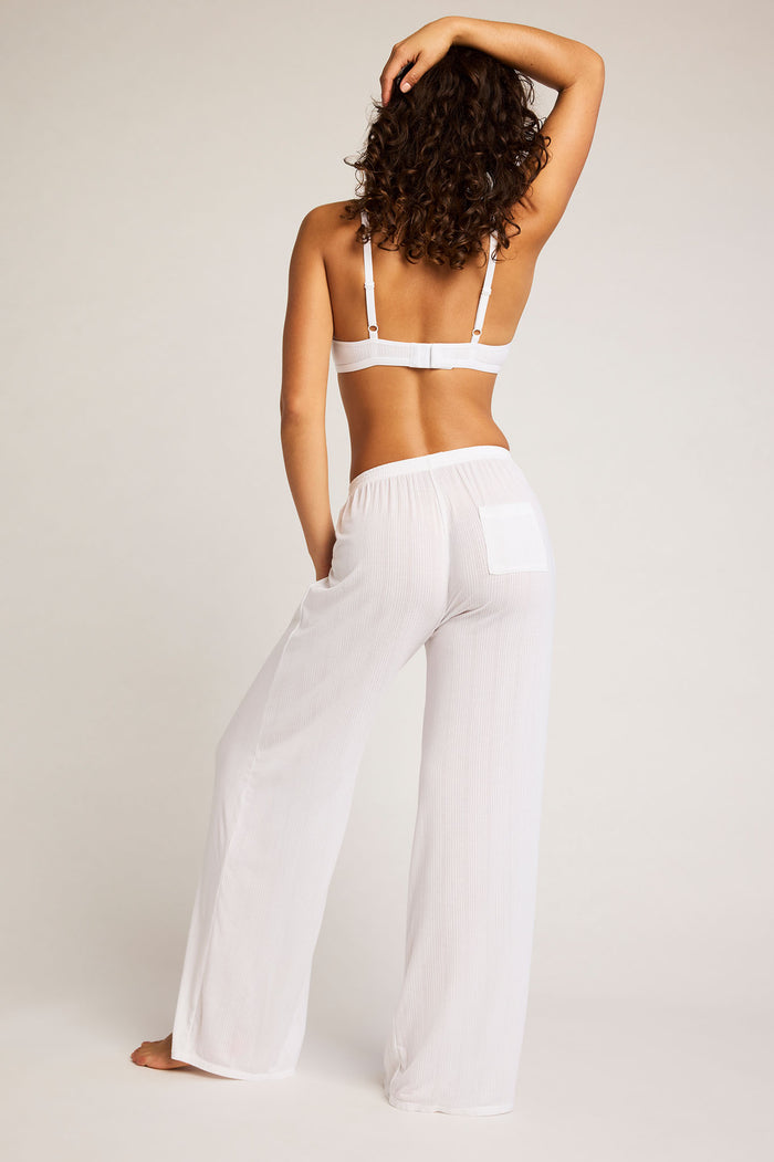 Back view of white wide-leg track pants with elastic waistband and drape fit